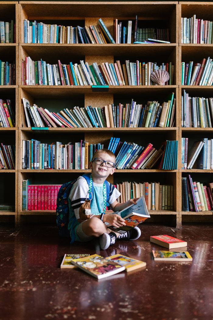 Mastering the First Impression: Your intriguing post title goes here A happy child with glasses enjoying a book in a library, surrounded by bookshelves.